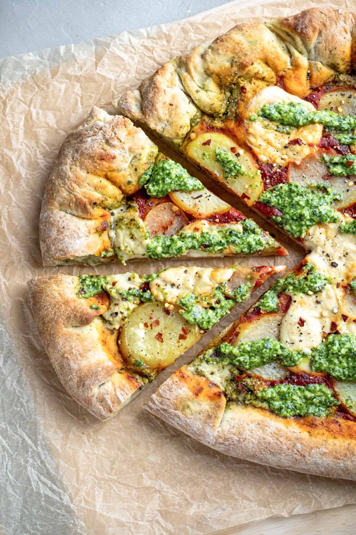 Vegan pesto and pottao pizza on a cutting board with two slices cut.