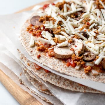 unbaked tortilla pizzas stacked with wax paper between each