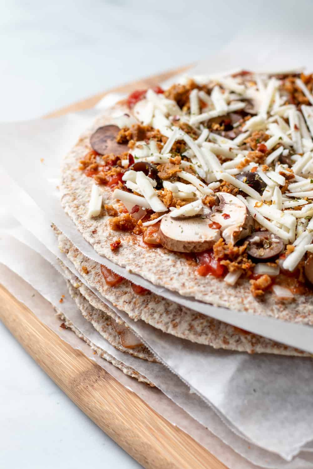 unbaked tortilla pizzas stacked with wax paper between each.