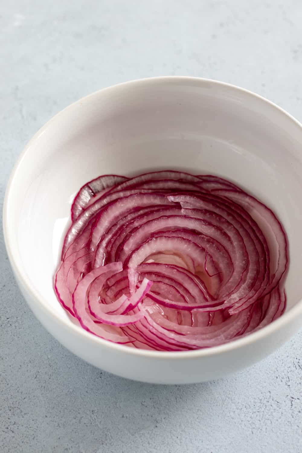 thinly sliced red onion marinating in rice vinegar - quick pickled onions.