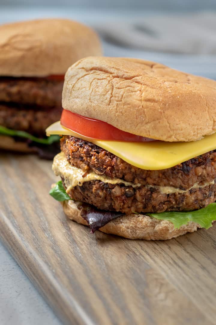 burgers on a bun with tomato, vegan cheese, lettuce and mustard.
