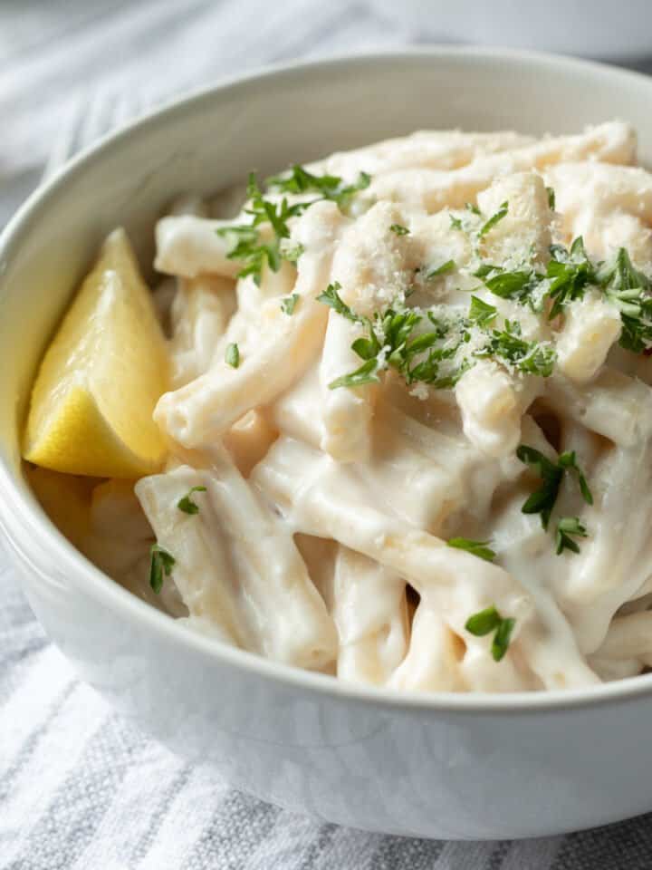 bright photo of creamy pasta in a white bowl with lemon.