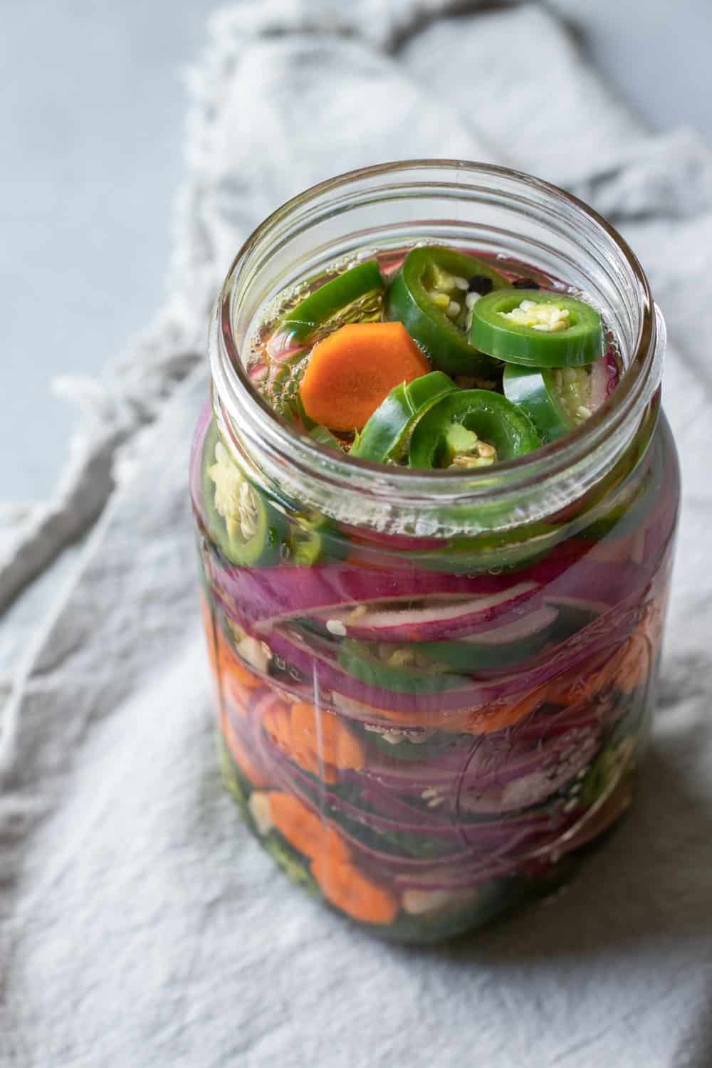 jar of spicy pickled jalapeños with carrot and red onion.