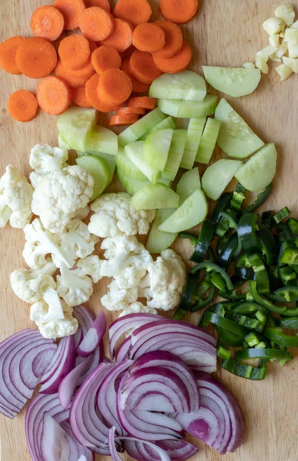 Chopping mixed vegetables for pickling, with carrot, cauliflower, cucumber, jalapeno and red onion on a cutting board.