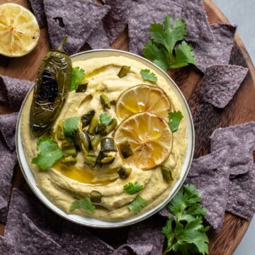 hummus on a wooden serving tray with chips, cilantro and roasted limes