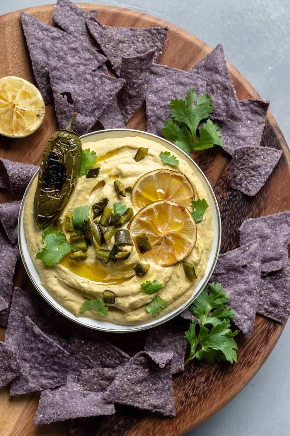 hummus on a wooden serving tray with chips, cilantro and roasted limes