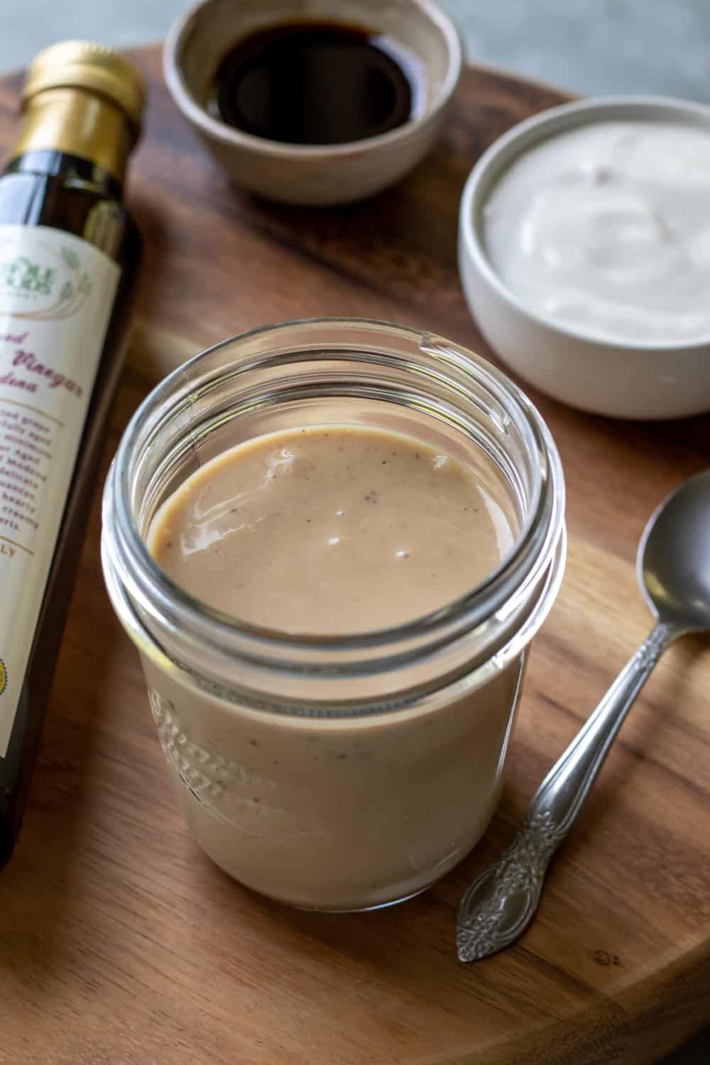 jar of dressing on a wooden board with a bottle of balsamic vinegar.