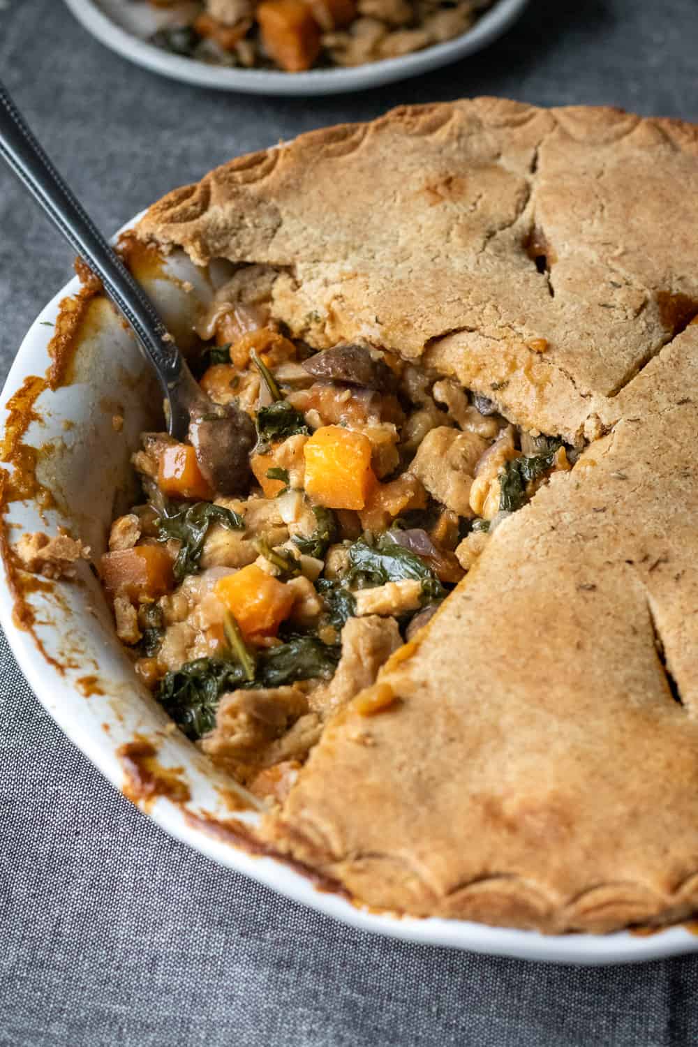 A spoon digging into vegan pot pie with a section of crust cut away to show the filling.