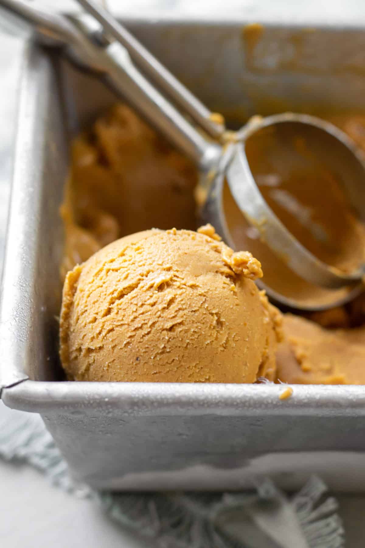 a scoop of pumpkin ice cream in a frosty metal loaf pan with an ice cream scoop resting behind.