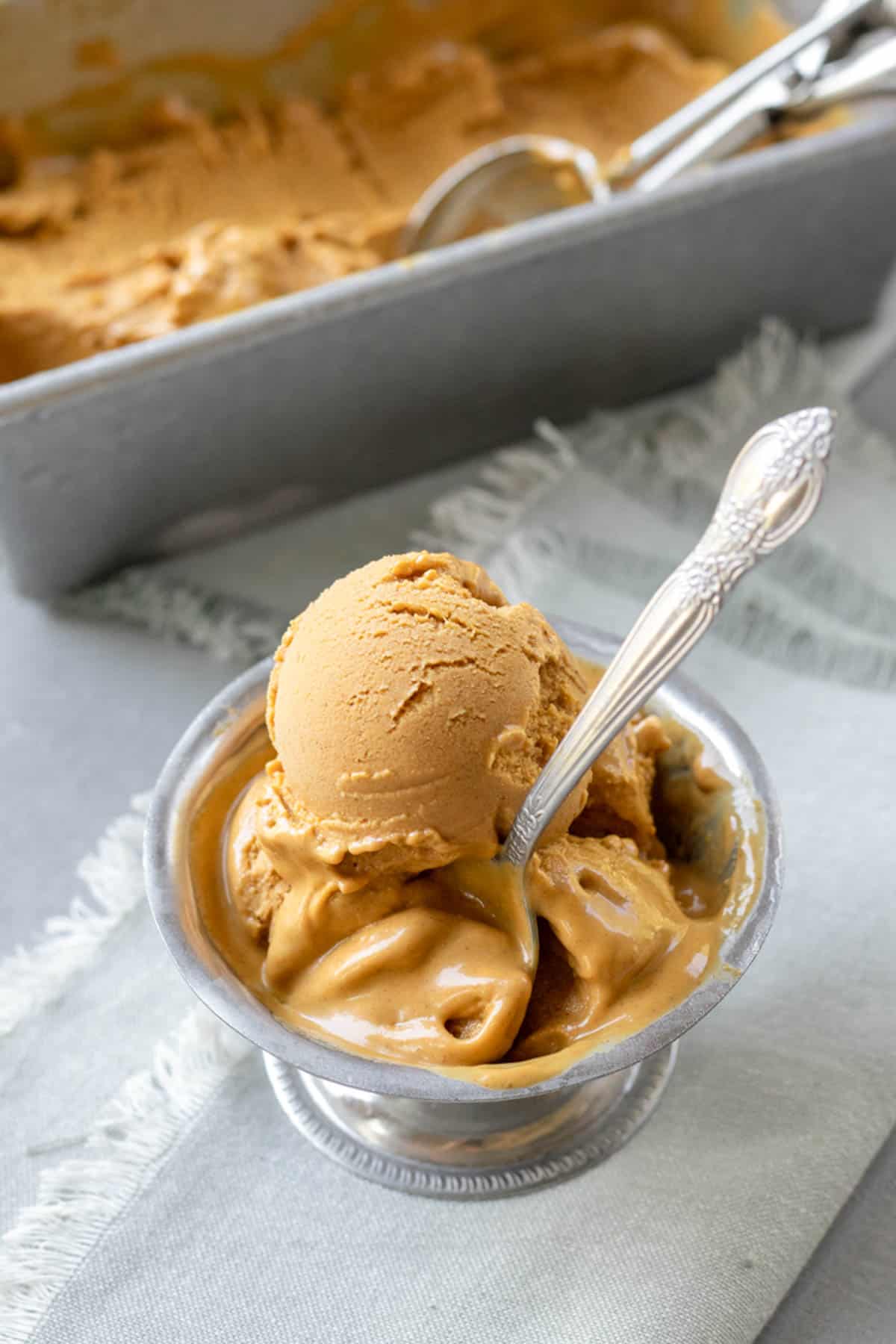 3 scoops of very creamy, melting pumpkin ice cream in a silver dish.