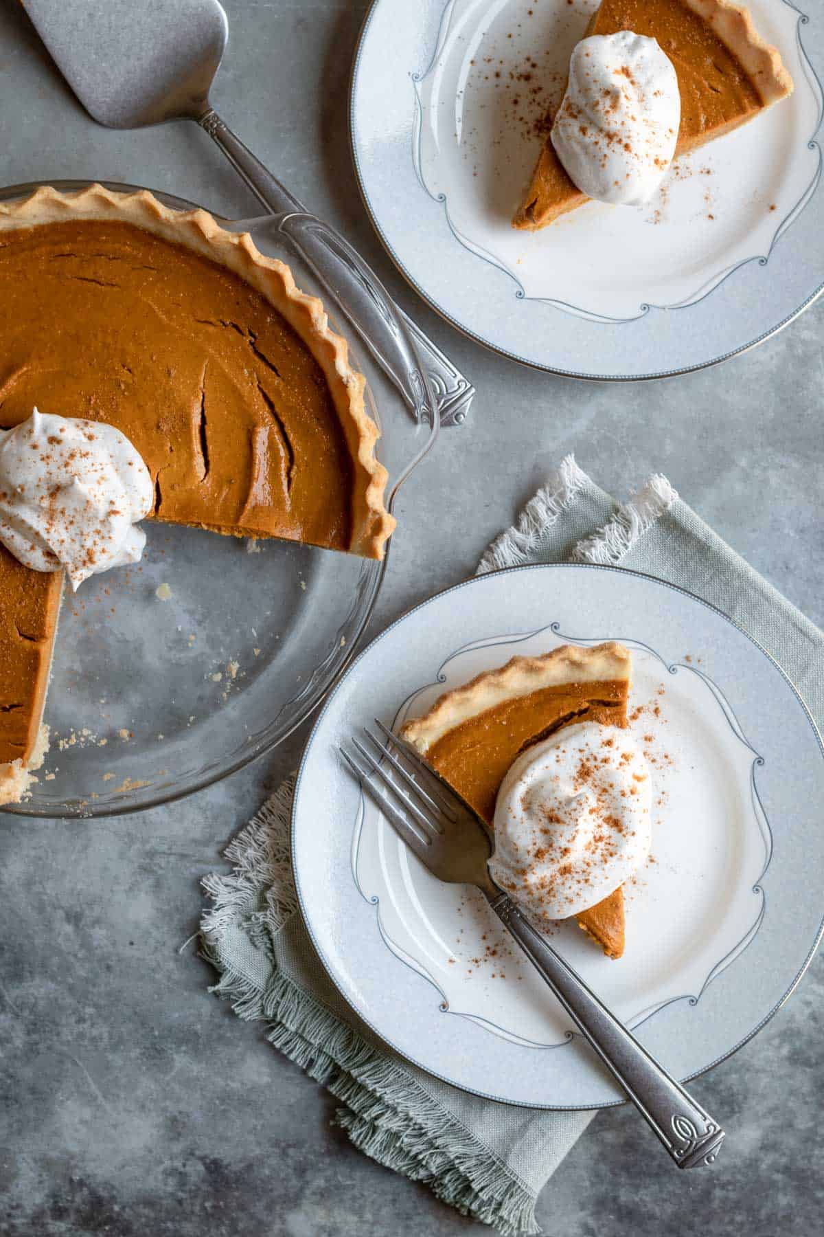 healthy pumpkin pie and 2 slices on plates with vegan whipped cream.