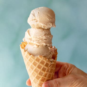 hand holding a waffle cone filled with 3 scoops of vegan ice cream.