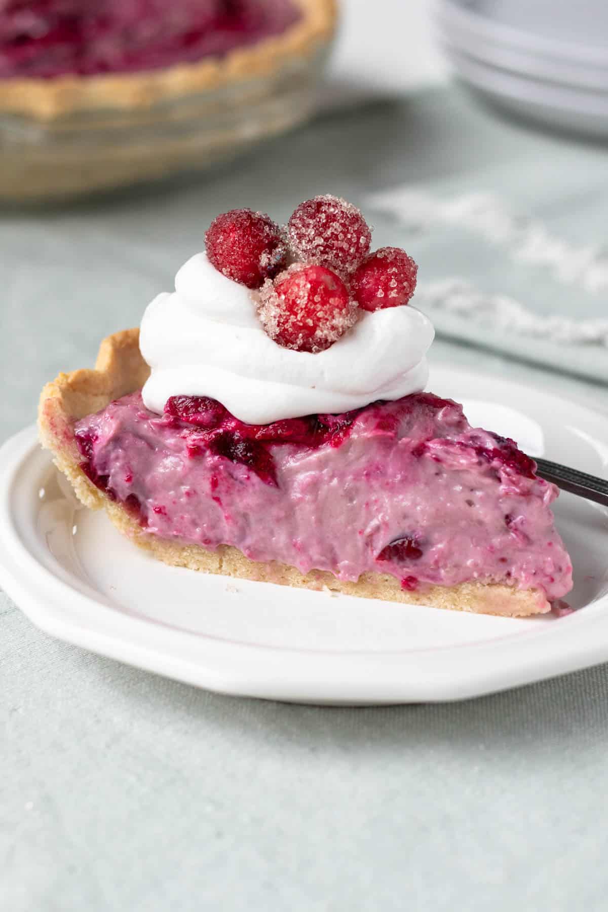 a slice of creamy cranberry pie topped with vegan whipped cream and sugared cranberries.