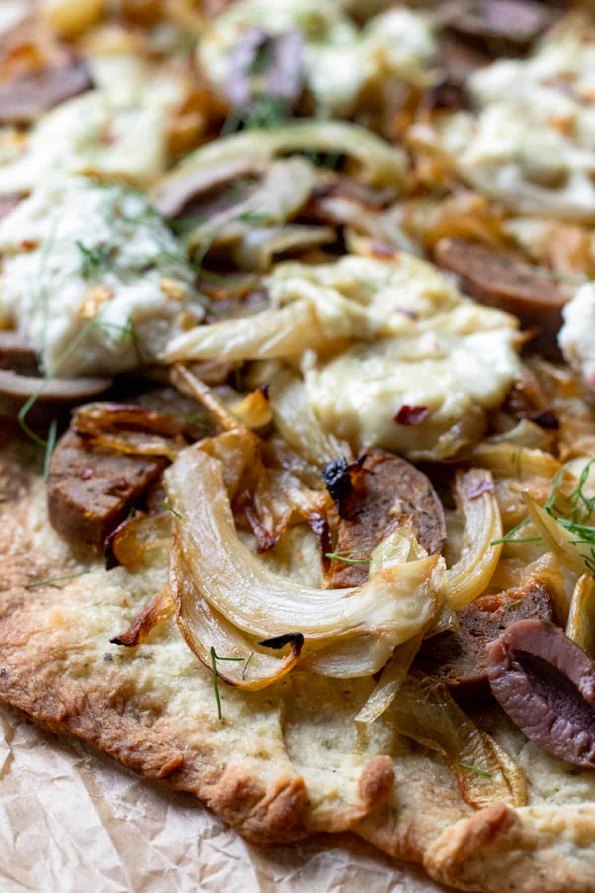 close up of vegan pizza with fennel, onion, sausage, and homemade non-dairy cheese.