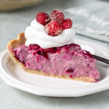 looking at the side of a slice of pie on a small white plate topped with whipped cream.