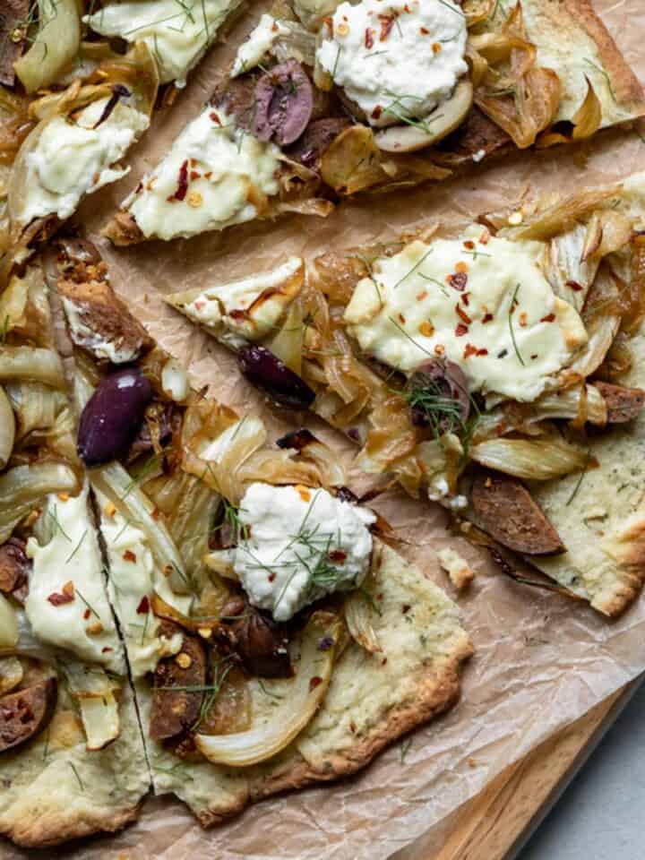 close up of sliced pizza topped with vegan ricotta, sausage, fennel and onion.