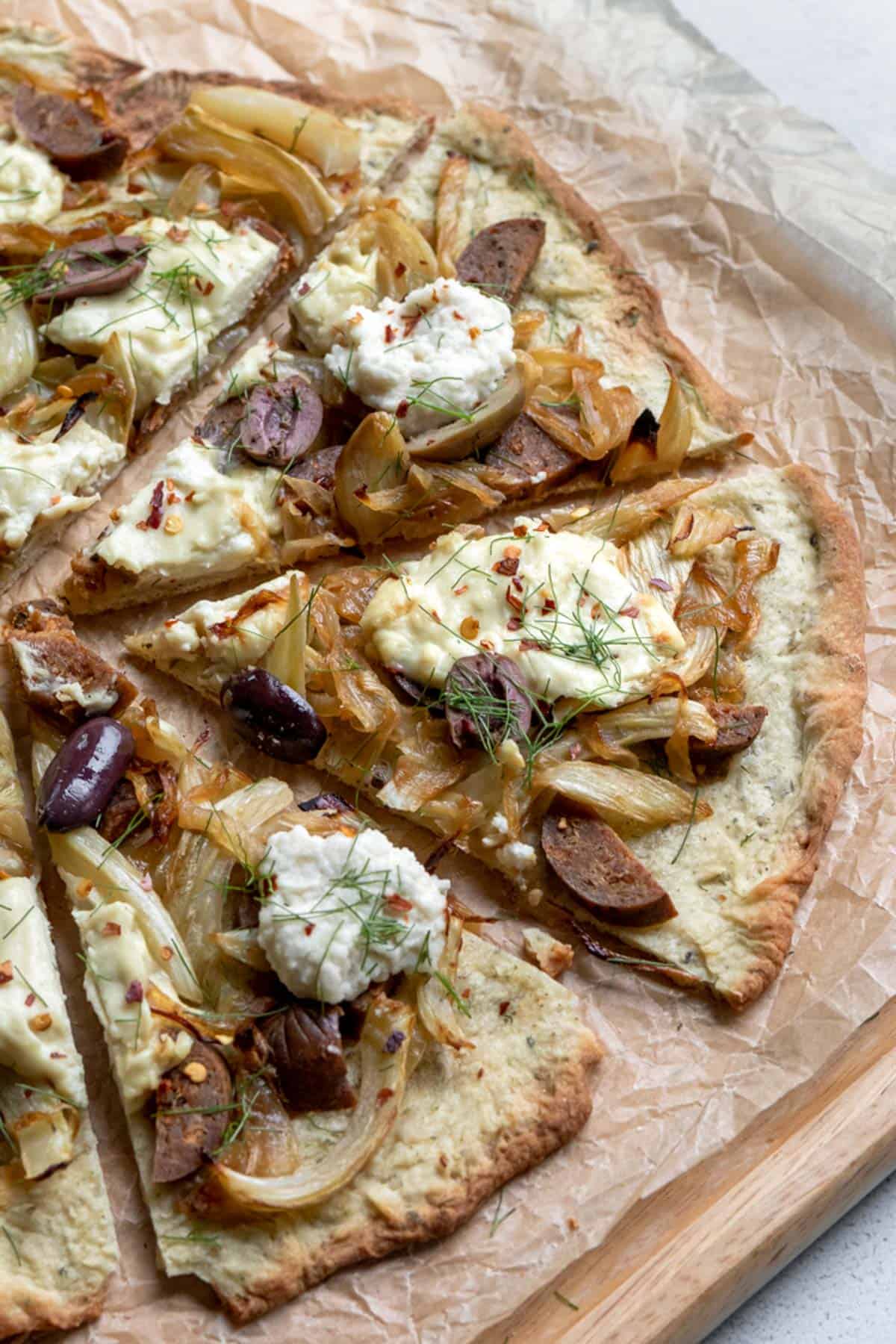 slices of vegan fennel pizza topped with dollops of ricotta on a cutting board.