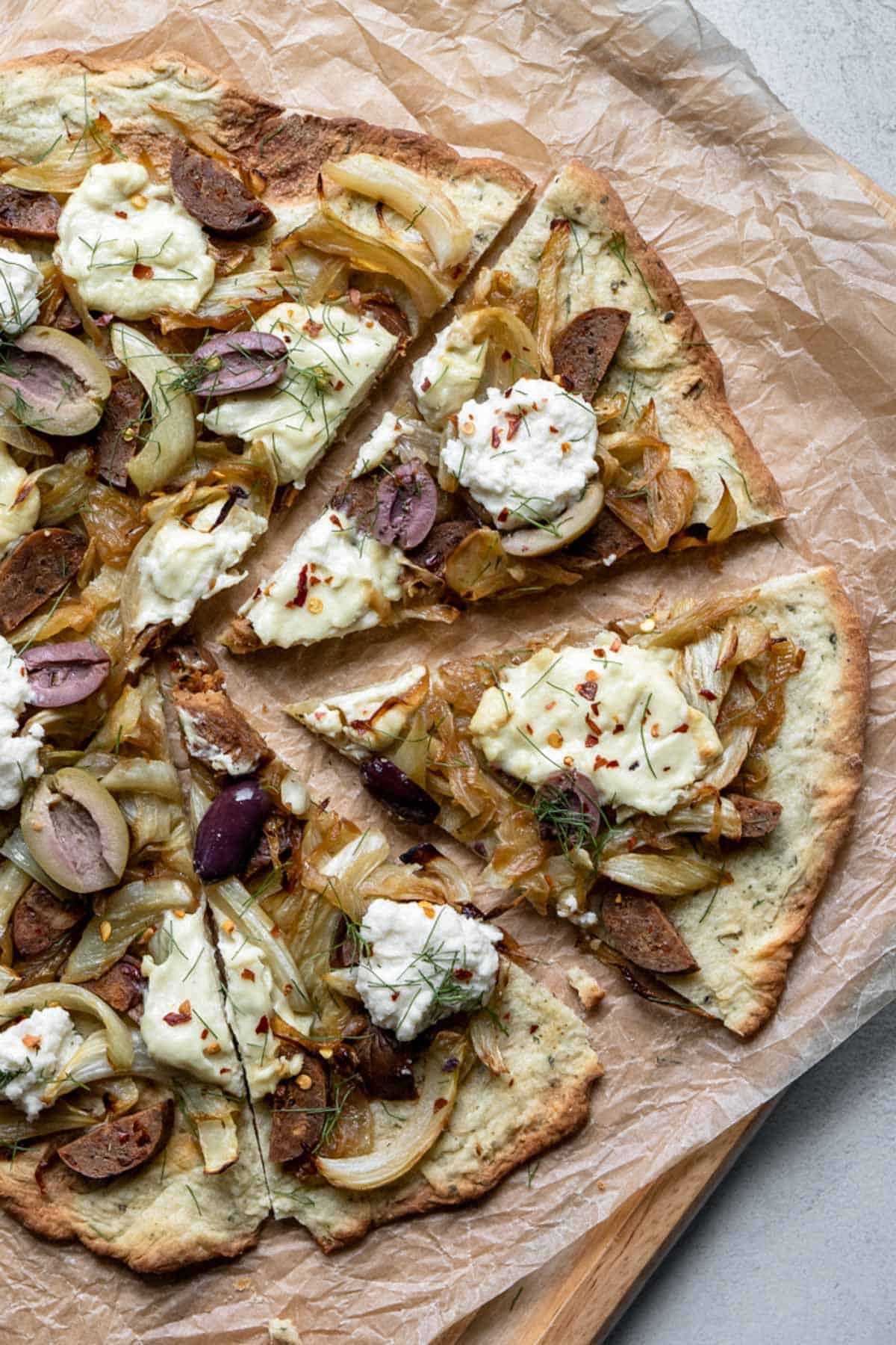 fennel and ricotta pizza with olives and sausage on a cutting board.