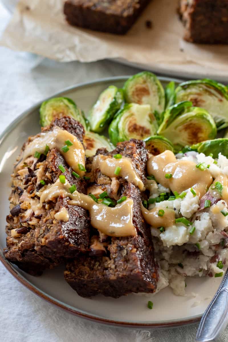 two slices of vegan meatloaf on a plate with mashed potatoes and Brussels sprouts.