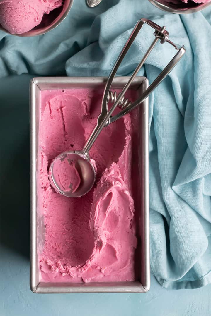 an ice cream scoop and cranberry oat ice cream in a pan.