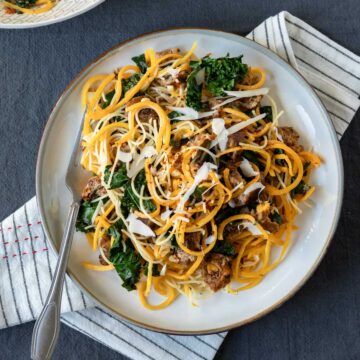 Spiralized butternut squash noodles with kale and sausage on a plate.