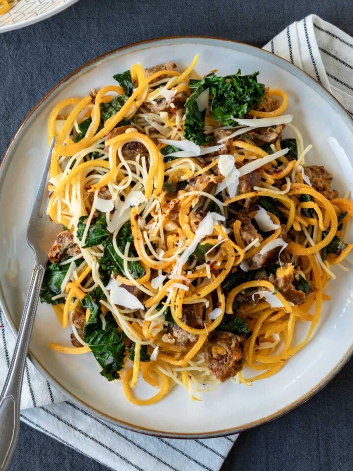 Spiralized butternut squash noodles with kale and sausage on a plate.