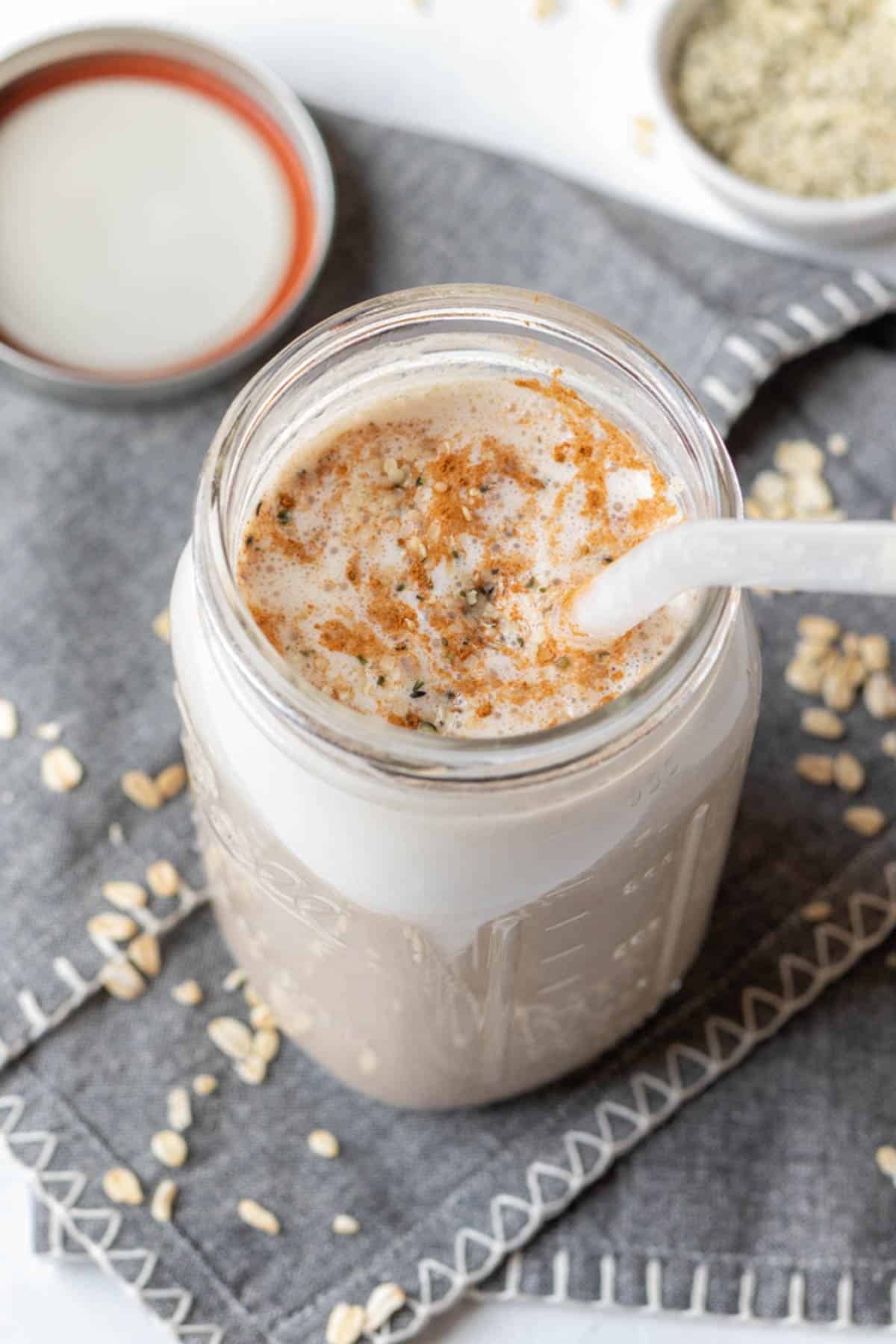Creamy oat drink topped with cinnamon in a large glass Ball jar with a glass straw.