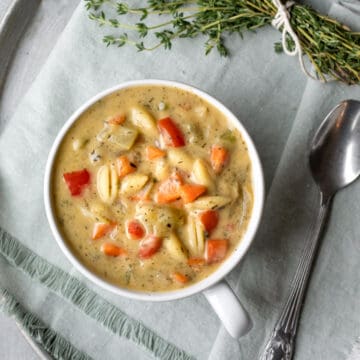 healthy and creamy vegetable noodle soup in a white bowl with herbs nearby.