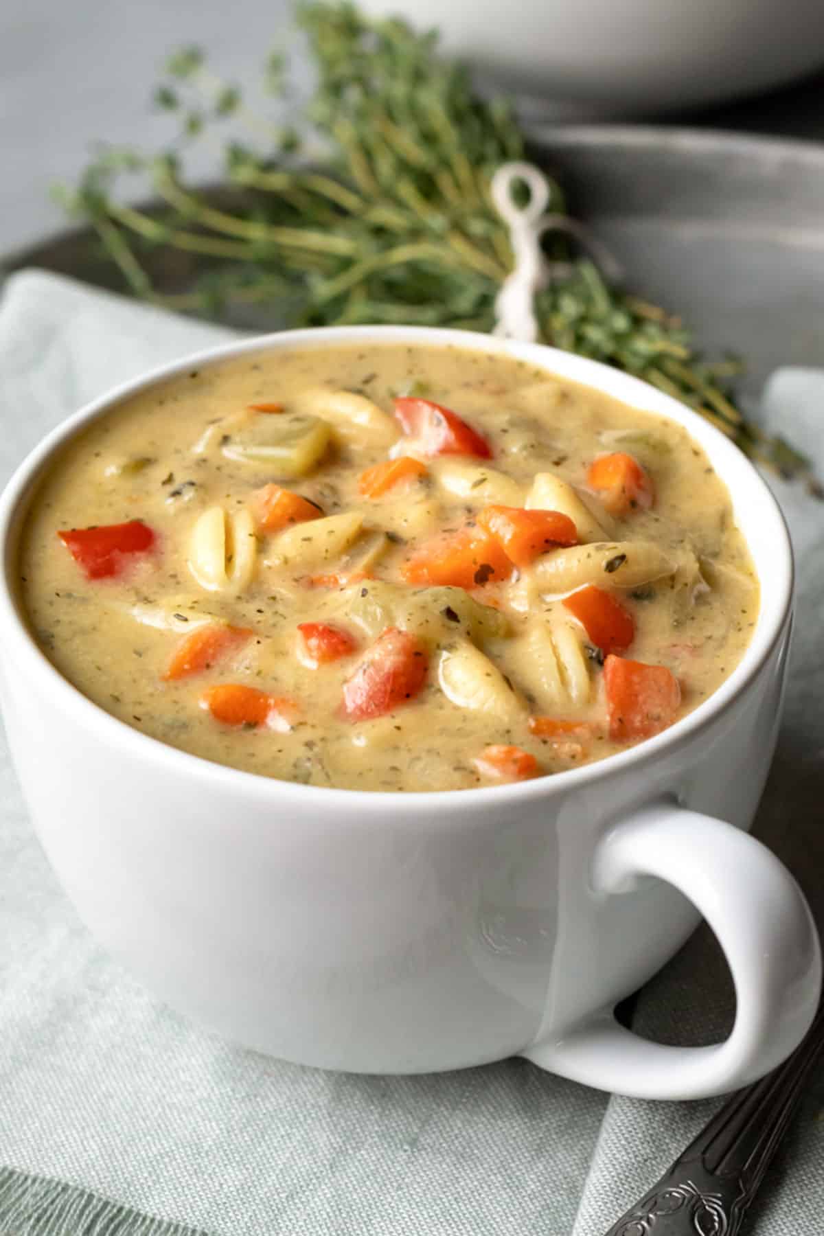 colorful and creamy vegetable noodle soup in a large white mug.