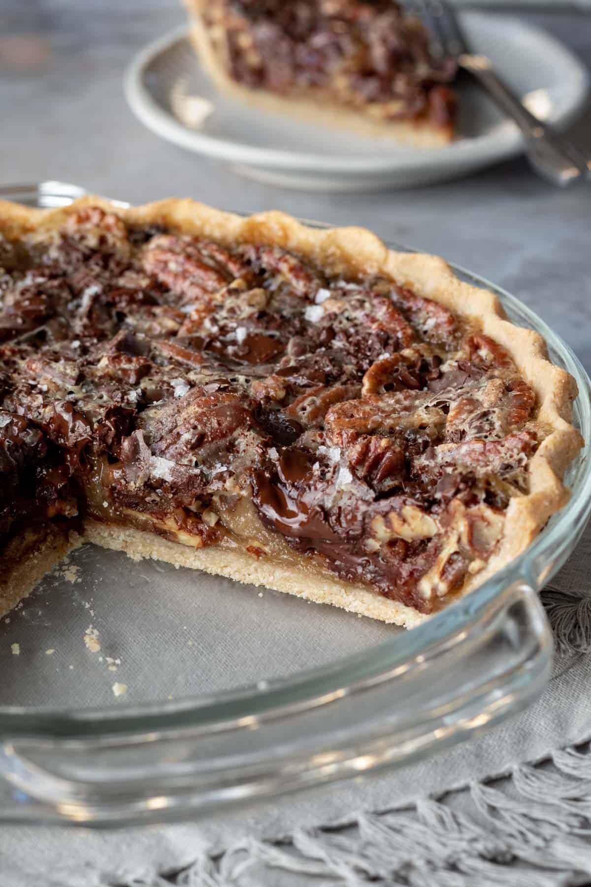slices have been removed from the pie in the dish showing the interior texture with pecans and melted chocolate.