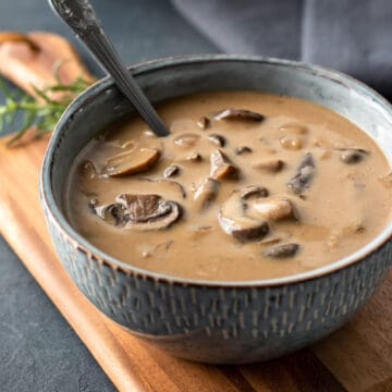 vegan mushroom soup in a blue bowl with chunky slices of baby bella visible on top.