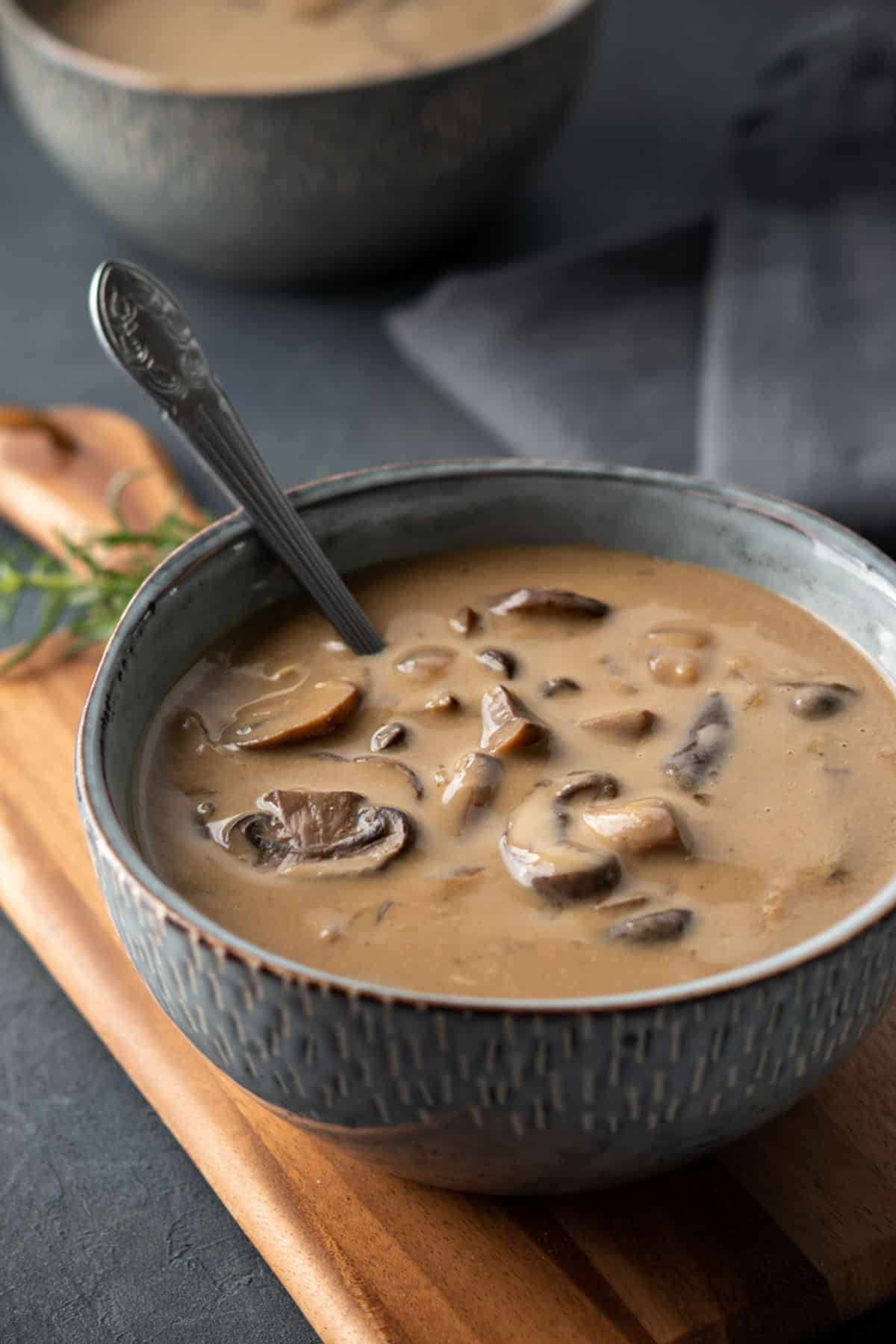 a bowl of thick and creamy mushroom soup on a wood cutting board.