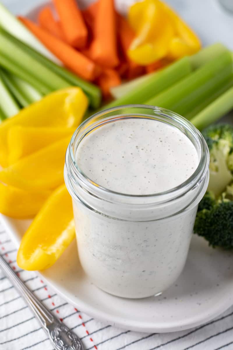 Creamy ranch dressing in a jar with veggies on a platter.