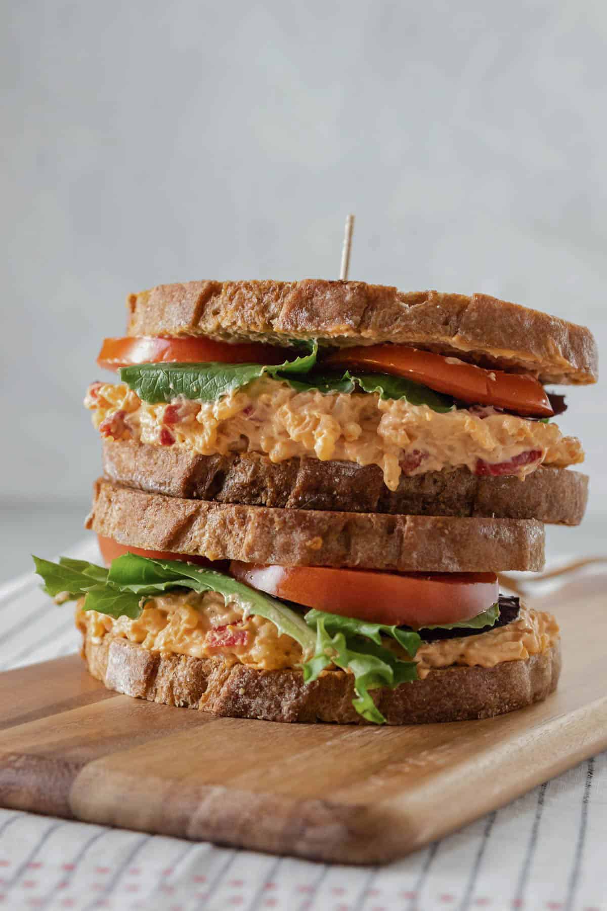 Two pimento cheese sandwiches stacked on a wood cutting board.