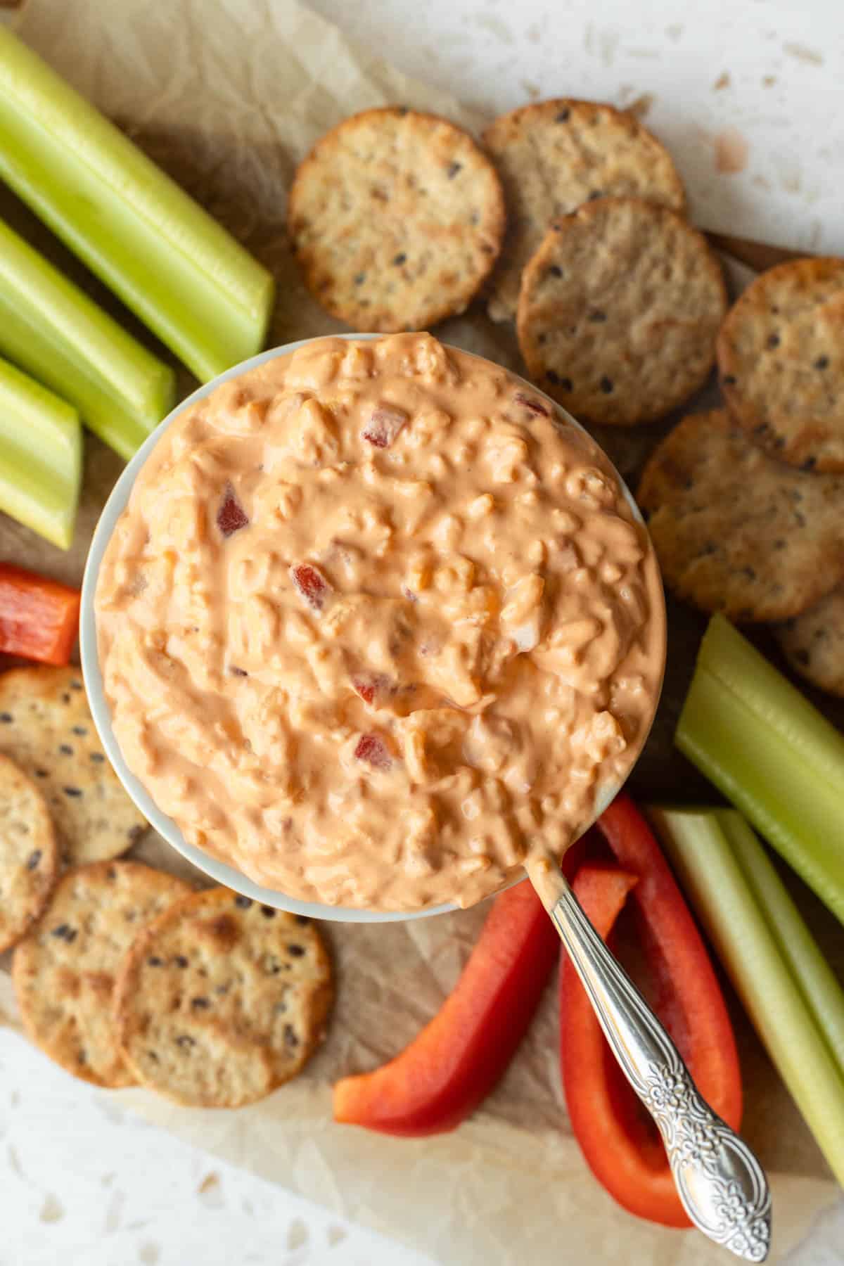 A bowl of vegan pimento cheese surrounded by raw veggies and crackers for dipping.