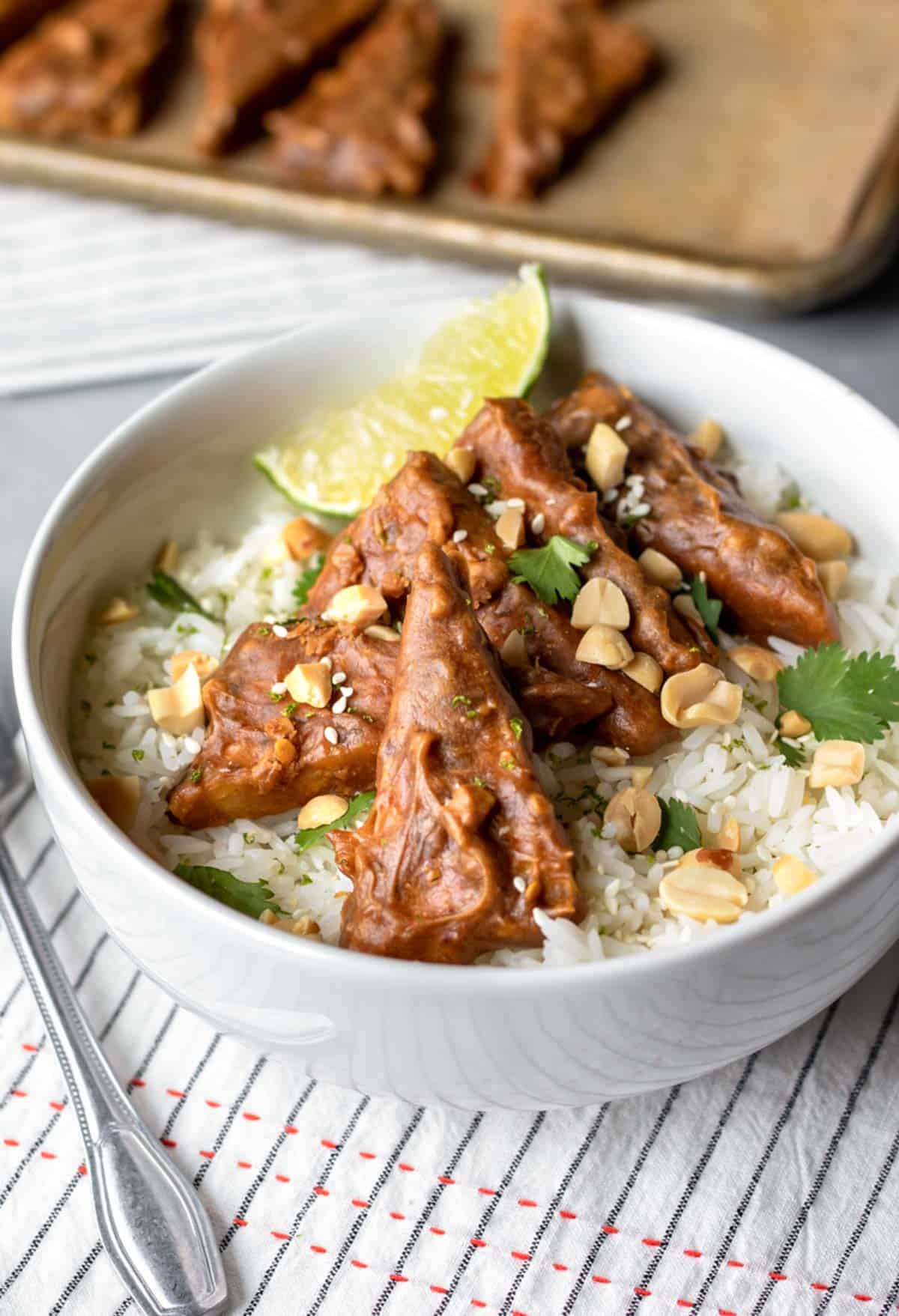 Easy baked peanut tempeh in a bowl with white rice and lime wedge.