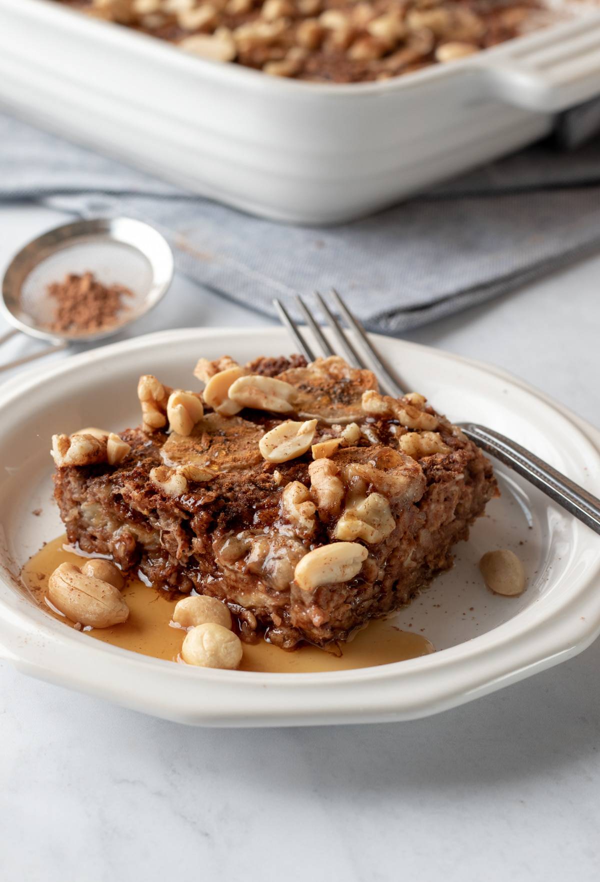 Chocolate banana baked oats on a white plate drizzled with maple syrup.