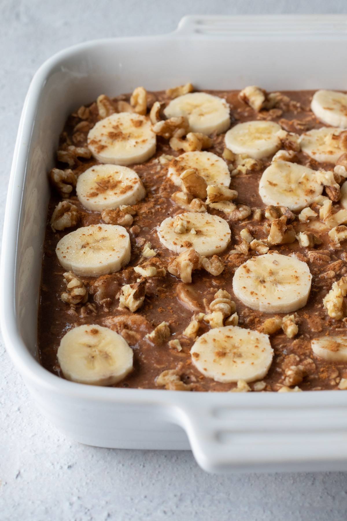 before baking, oatmeal mixture topped with slices of banana and crumbled walnuts.