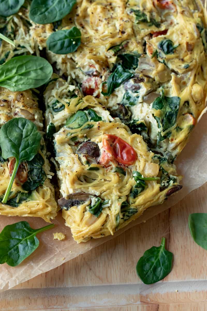 close up of a slice of vegan tofu frittata with spinach, mushroom and tomatoes peeking through