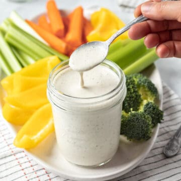 a hand dipping a spoon into a jar of oil-free vegan ranch dressing.