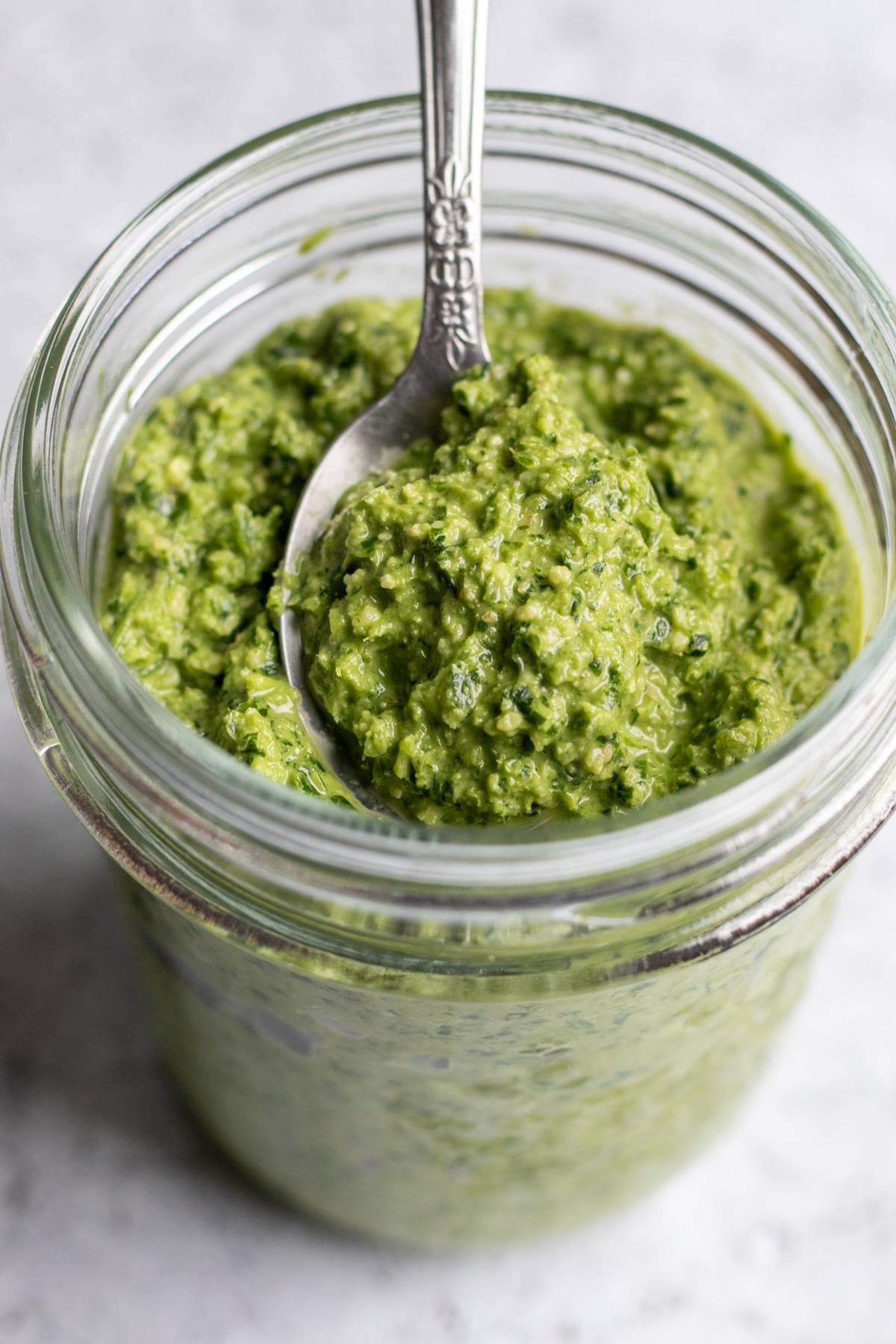 parsley pesto in a glass jar scooped up with a small spoon.