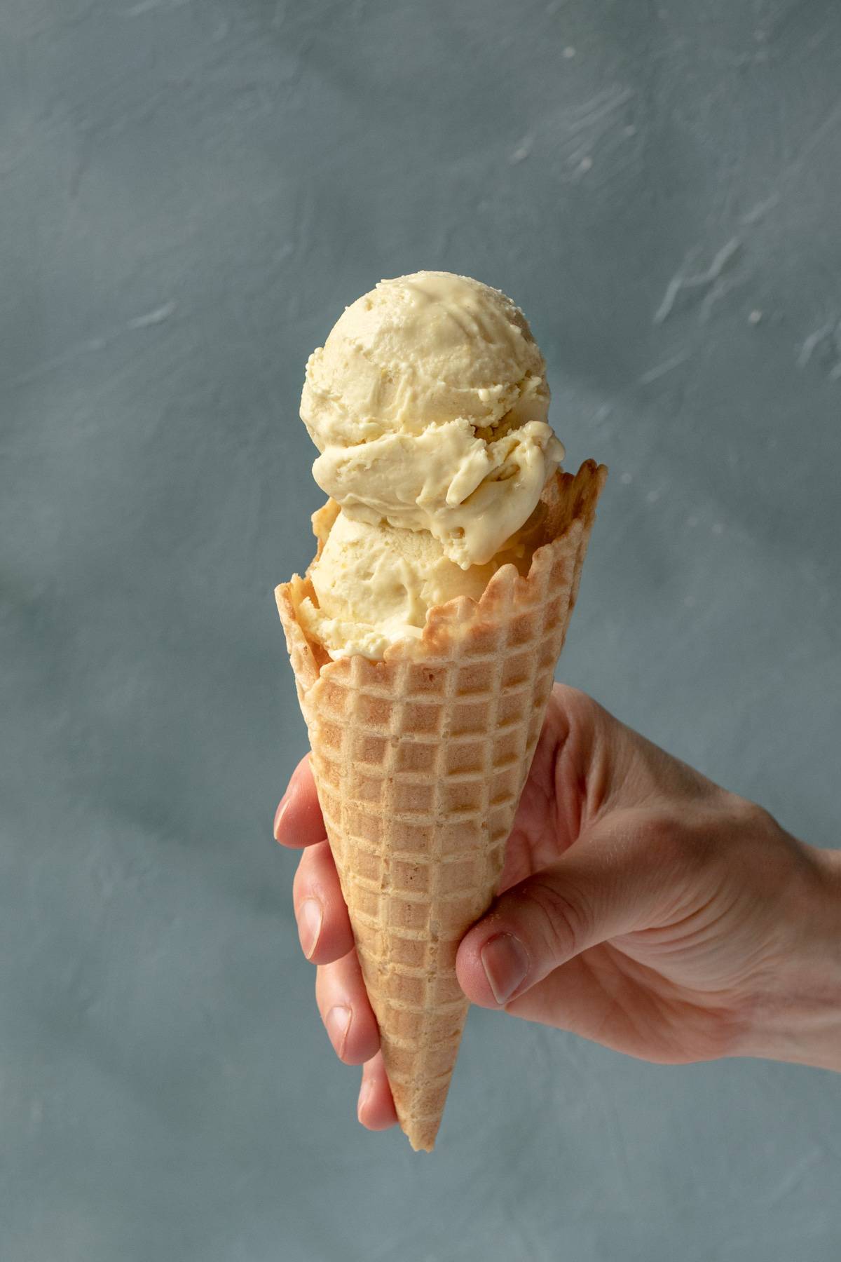 a hand holding an ice cream cone against a blue background.