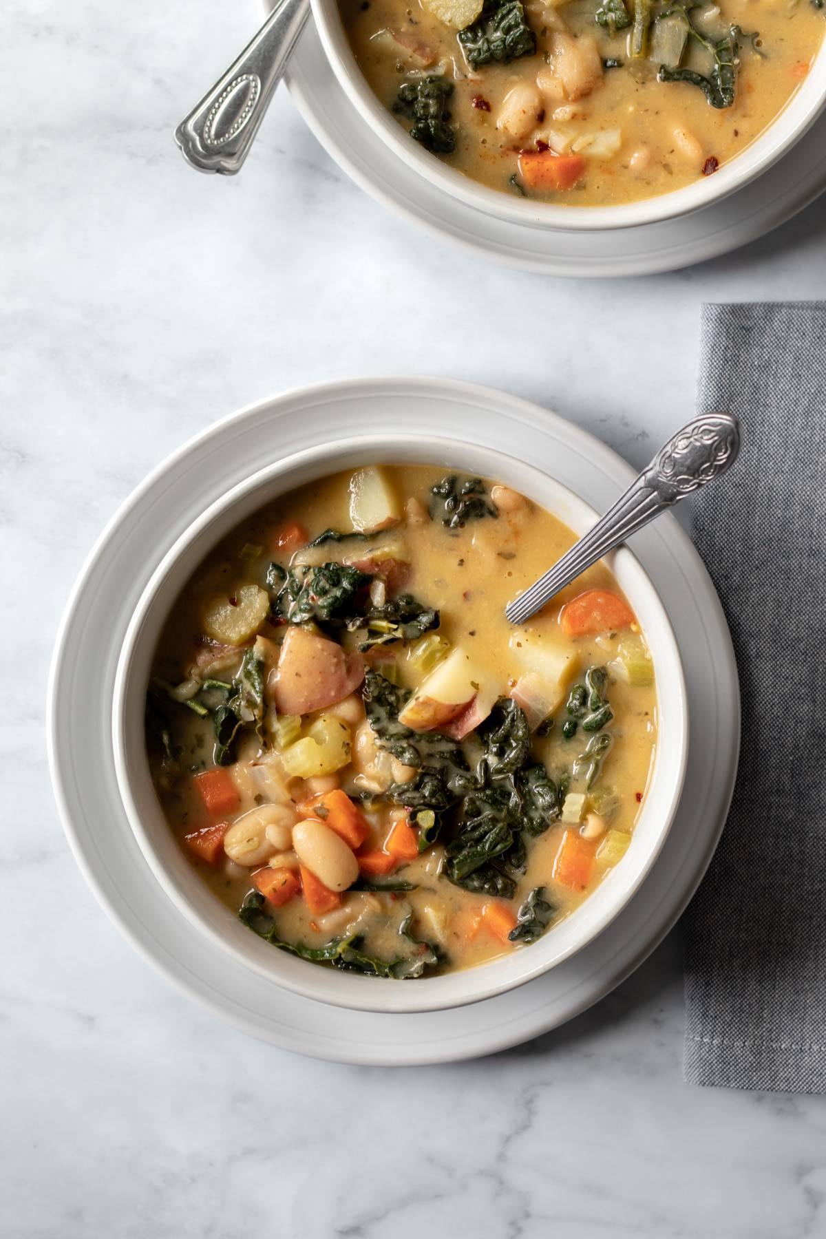 two servings of creamy Tuscan soup in bowls on a marble surface.