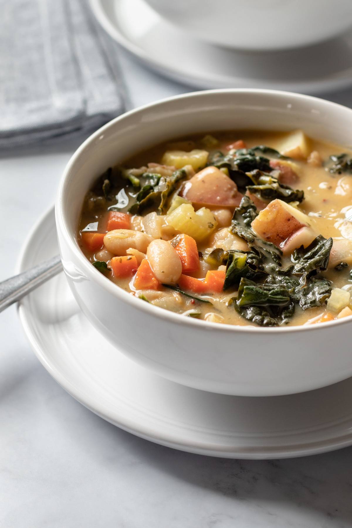 a bowl full of creamy Tuscan bean soup with kale, cannellini beans, potatoes, and veggies.