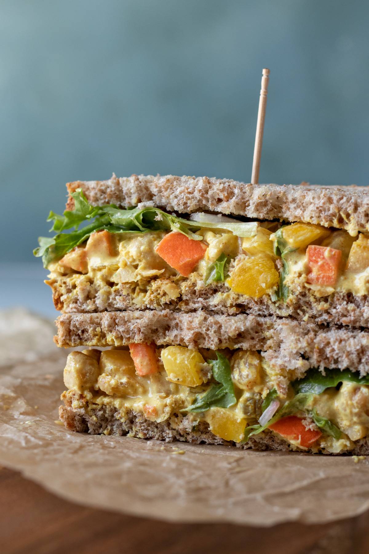 a colorful curried chickpea salad sandwich cut in half to show all the veggies inside.