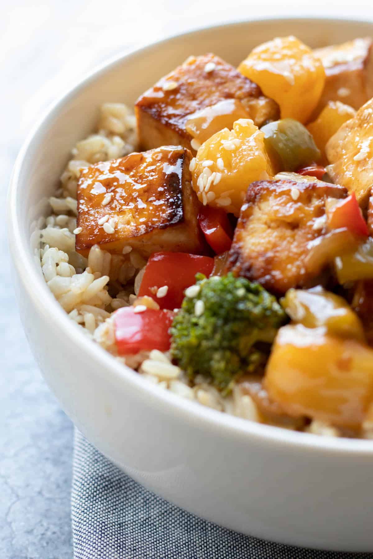 Sweet and sour tofu and veggies on top of rice in a white bowl.