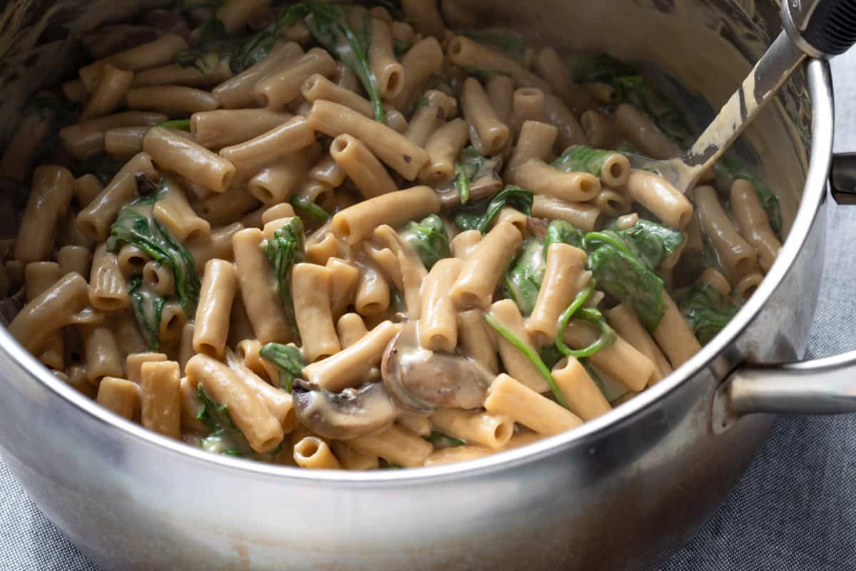 stirring together mushroom sauce, spinach, and cooked pasta in a large pot.