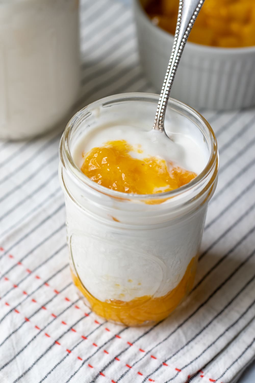 small jar of cashew yogurt with a larger jar of yogurt and mango compote in the background.