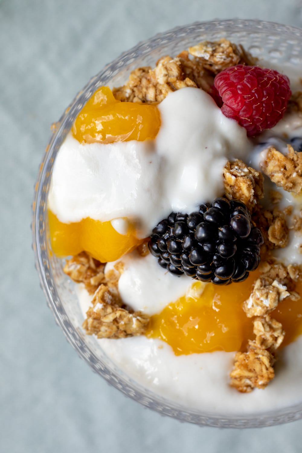 overhead view of yogurt, berries, and granola in a decorative glass bowl.