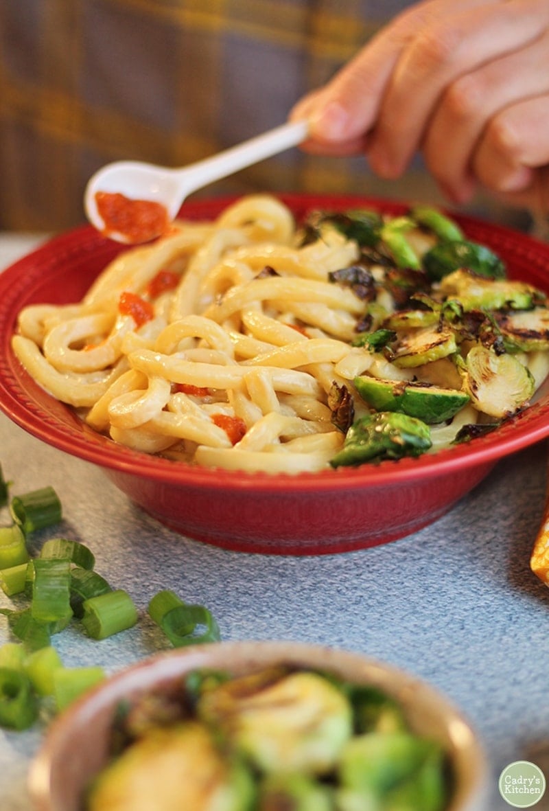 hand drizzling sriracha sauce onto udon noodles.